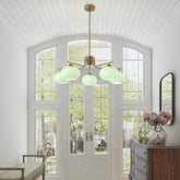 Chandelier with green glass shades in a room with large windows and a wooden cabinet.